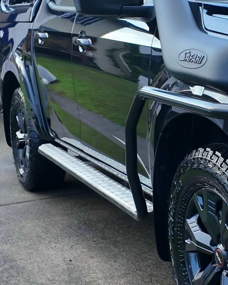 The flank of a black dual cab, the lawn mirrored in the doors.