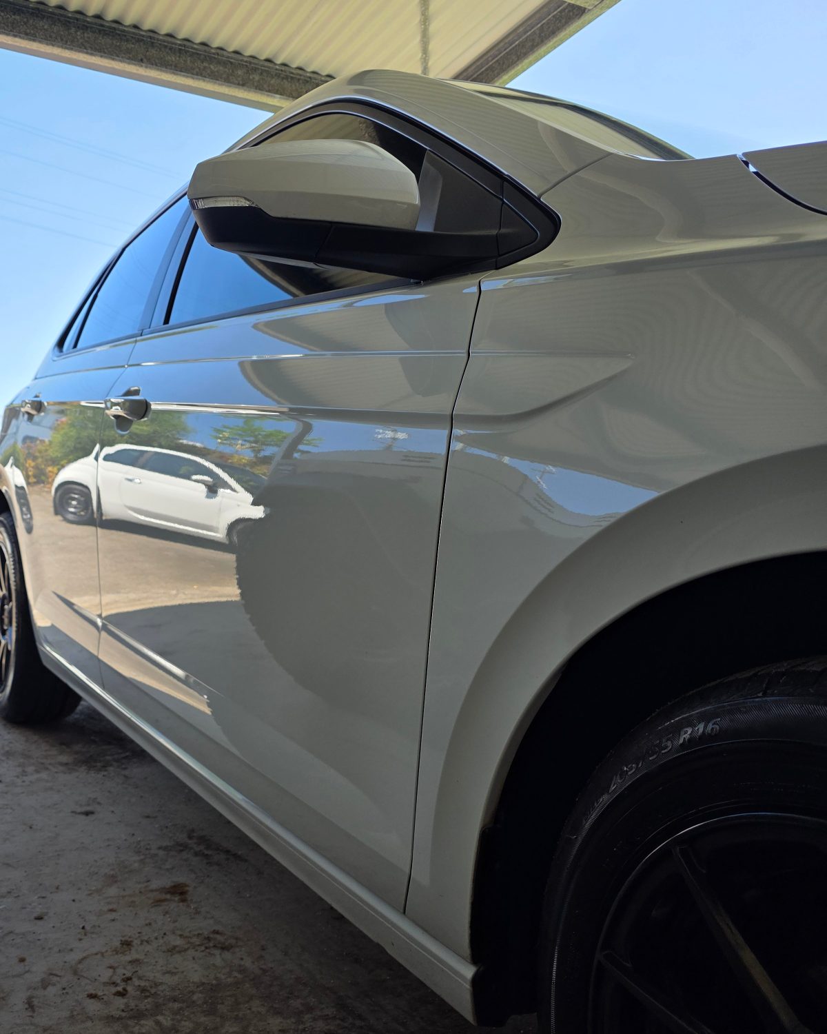 A car mirrored in the door panel of a finished sedan, the reflection sharp enough to read.